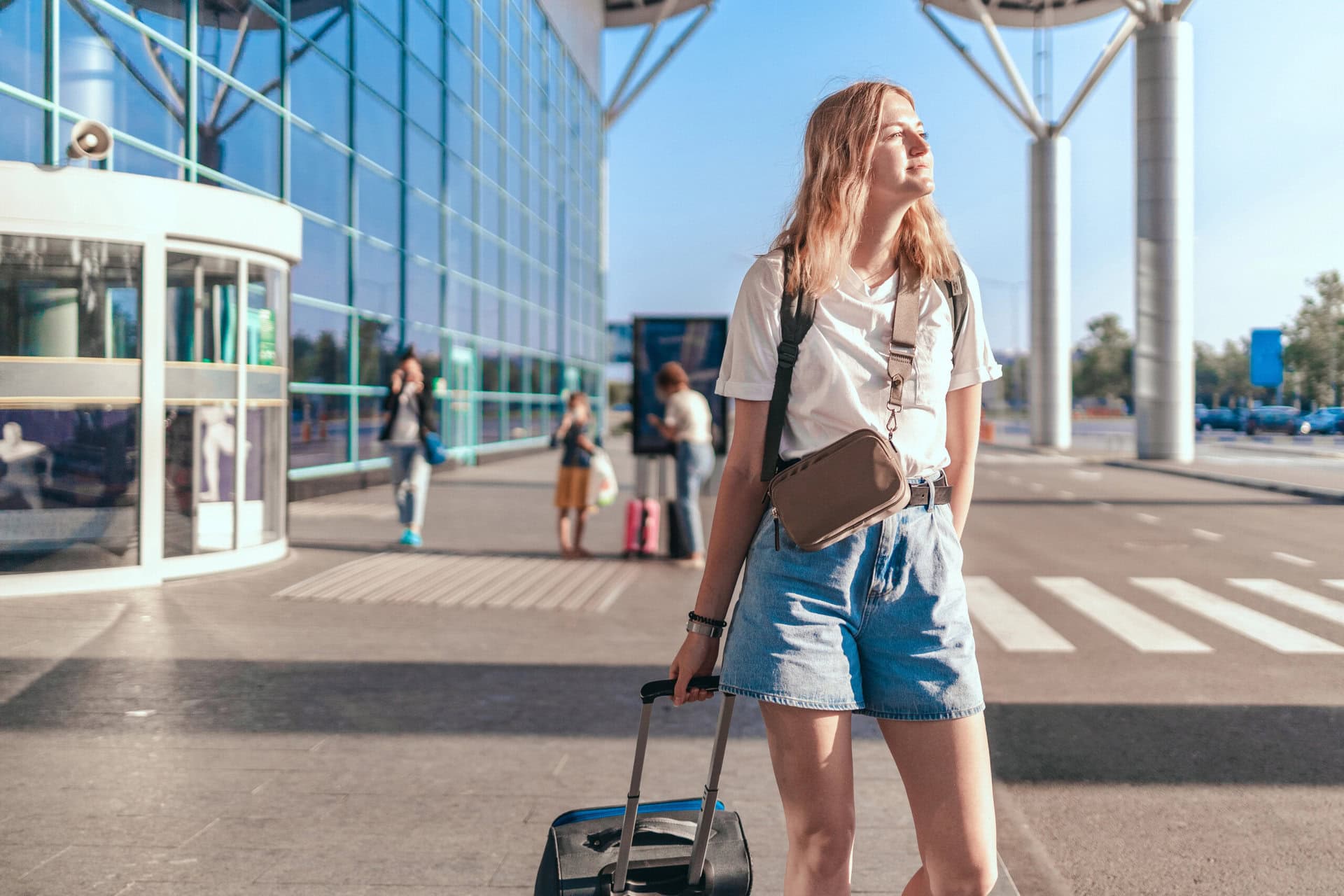 Travel woman tourist with backpack and hand luggage suitcase standing near international airport terminal waiting for boarding.